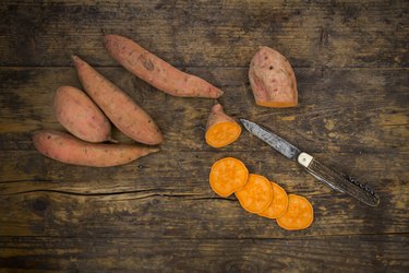 Sliced and whole sweet potatoes on dark wood