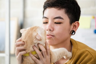 Close up shot of young Asian tomboy woman in casual attire holding and looking at her cat affectionately