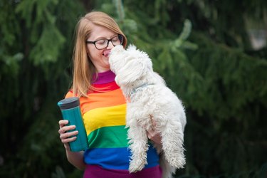 woman in rainbow sweater with cute white dog licking her face