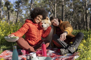 multiracial young couple and their dog camping in the woods on a beautiful sunny day; spend time outdoors and appreciate nature. rest and food