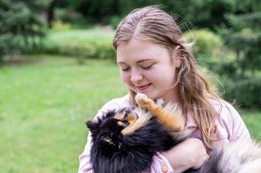 Portrait of young blond woman hugs her pet dog Spitz Pomeranian outside in park