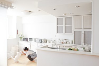 A woman playing with her white cat in a kitchen.