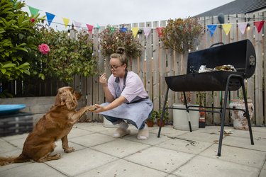 Woman holding a dog's paw, they are outside by a grill