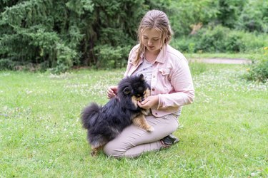 Young blond woman trains and feeds her pet dog outside in park