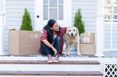 Woman sitting with her labrador on her porch with moving boxes.