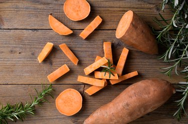 Raw whole orange sweet potato and slices of batatas with fresh rosemary on rustic wooden background, flatlay