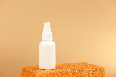 White spray bottle on golden block and gold background.