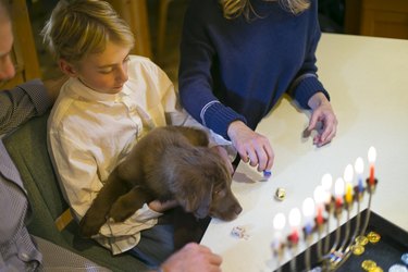 A boy holding a lab puppy and spinning dreidels with his family at Hanukkah.