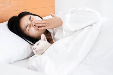 Asian woman sleeping with cat having allergic to cat fur and sneezing in bed