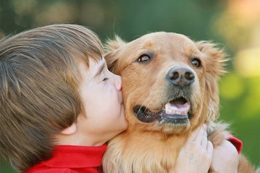 A young boy kissing and hugging a golden retriever