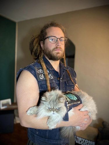 Man and cat pose together with matching denim vests.