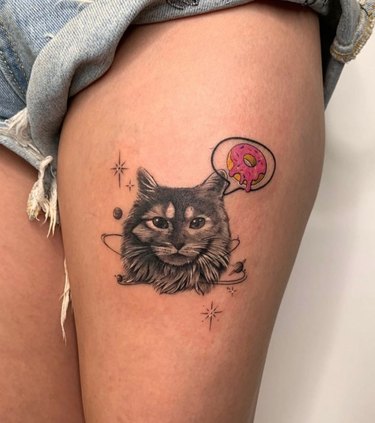 A tattoo of a cat thinking about an iced donut.