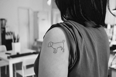 An outline of a dog tattoo on a shoulder.