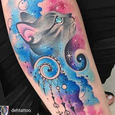 A tattoo of cat's face with cosmic blue, purple, and pink flourishes.