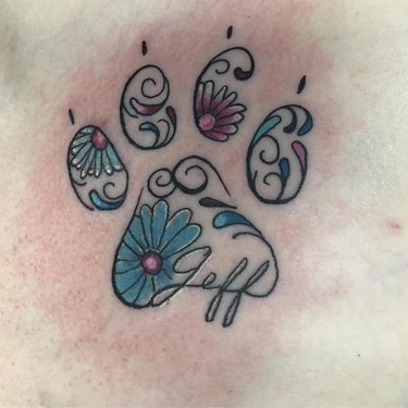 A tattoo of paw print with flowers and the name "Jeff" incorporated in the design.