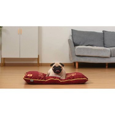 A pug resting on a red Fetch For Pets Harry Potter Napper Dog Bed with a Hogwarts crest design