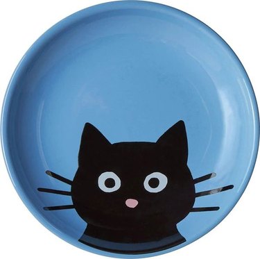 Blue ceramic dish with cartoon black cat face with whiskers and pink nose.