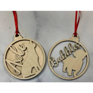 Two laser cut ornaments with an outline of pets and the pet's name
