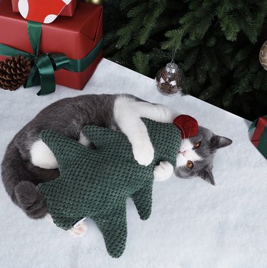 Cat playing with a plush Christmas-tree shaped pillow.