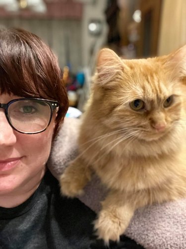 cat laying on woman's shoulder with a towel