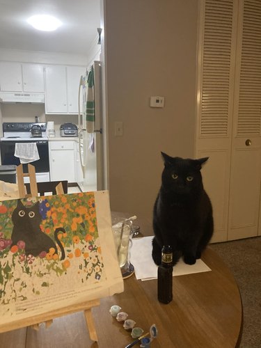 black cat standing next to painting of black cat.
