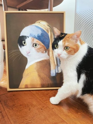 Calico cat posing in front of a cat version of the famous painting, Girl With the Pearl Earring.