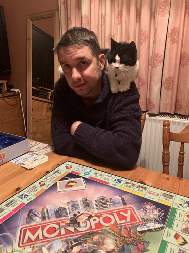 cat on man's shoulder playing monopoly