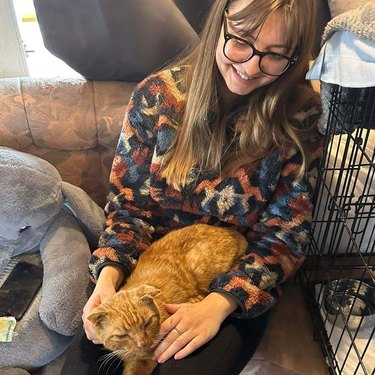 Ginger cat from a shelter sleeps on woman's lap.