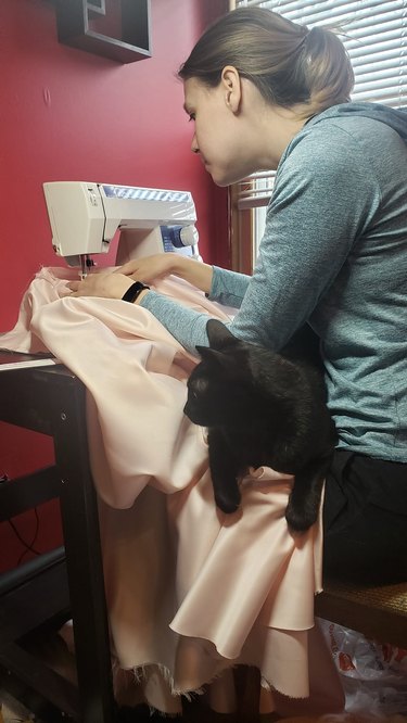 Black cat sitting on woman's lap while she is sewing.