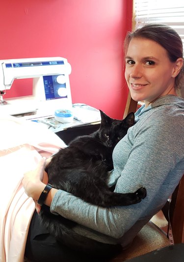 Black cat insists on cuddling with woman while she is sewing.