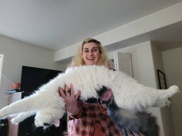 Woman holds very long black and white cat that is stretched out with their back arched.