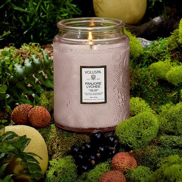 A large pink glass candle sitting among greenery and berries.