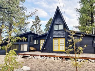 Navy blue A-frame cabin with bright yellow glass pane double doors and a level front deck.