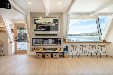 Living room with expansive windows with lake views, a large TV, fireplace, and bar seating along the window.