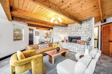 Living room with wood beam ceiling, large stone fireplace, and modern furniture.