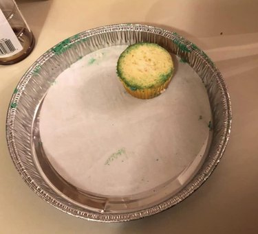 A cupcake in a tin is without a top with green frosting.