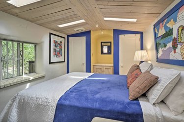 Bedroom with natural wood ceiling and a bright blue and yellow accent wall with bedding to match.