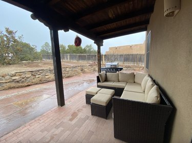 Covered patio with terracotta tile and an outdoor sectional overlooking the fenced-in mostly dirt backyard.
