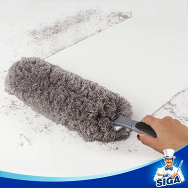 a washable duster cleaning up dirt on a white surface.