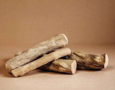 Canophera coffee wood dog chews in a pile, all various sizes, against a terracotta colored background.