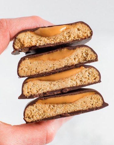A person's thumb and pointer finger holding a stack of cookies with chocolate on the outside and peanut butter on the inside.
