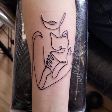 A single minimalist line tattoo of a woman holding a cat.