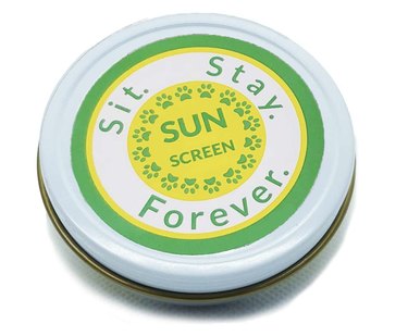 SIT. STAY. FOREVER. Organic Sunscreen in a metal tin that's white, yellow and green. The tin is closed and pictured against a white background.