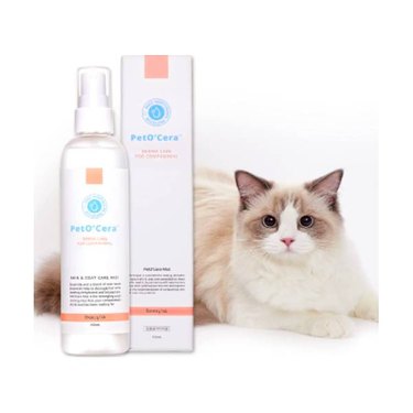 A bottle of Breezytail PetO'Cera Mist next to its box and a long-haired cat. The bottle has a spray head.