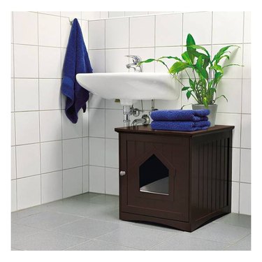 A brown wood TRIXIE Wooden Cat Home & Litter Box Cover with towels and a plant sitting on the top.