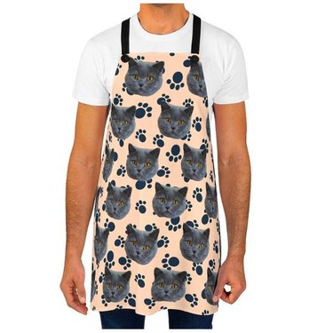 A man wearing an apron with a cat's face repeatedly printed on it and with paw prints in the background