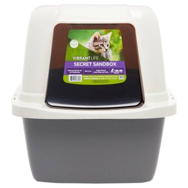 A Vibrant Life Secret Sandbox Cat Litter Box with a white hood, a gray base and a clear swinging door.