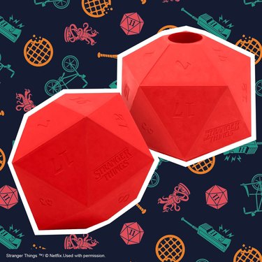 Two rubber 20-sided dice toys with a small hole at the top for inserting treats. The dice are red and have numbers and the "Stranger Things" logo etched into them.