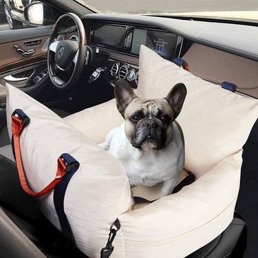 French bulldog sitting in Capeka Luxury Dog Car Seat and Travel Bed in the passenger seat of a car. The bed looks very fluffy and has handles for carrying as well as straps that attach it to the car seat.