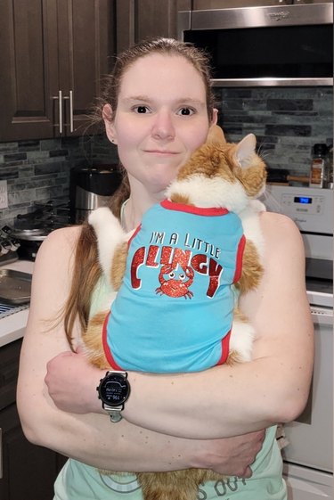 clingy cat in onesie holds onto woman